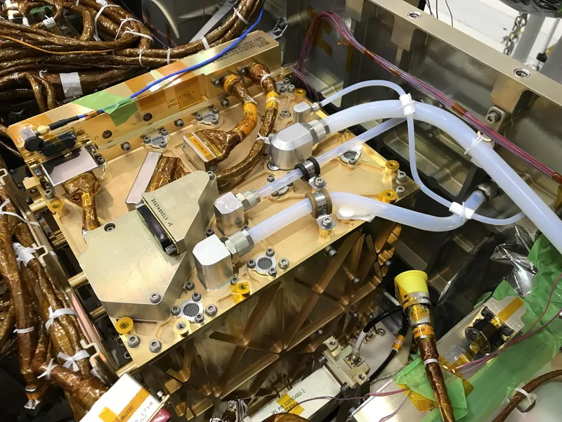 The gold-plated MOXIE oxygen experiment installed inside the Perseverance rover, with white intake and outlet tubes across its top